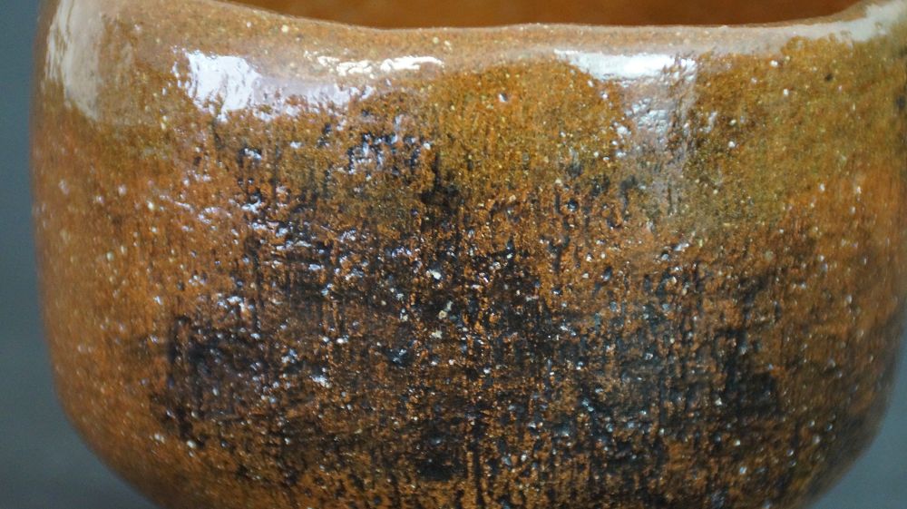 Primer plano extremo de la textura granulada del esmalte marrón miel del chawan de cerámica de Ohi