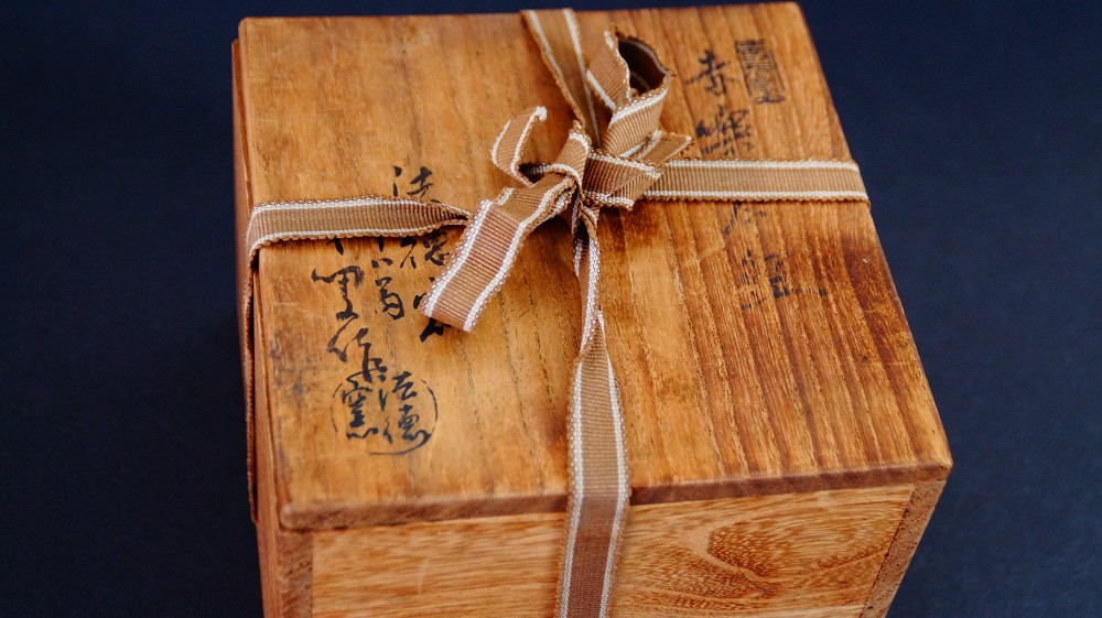 Caja de conservación cerrada del chawan de cerámica Raku por Sairi Hotoku con inscripción a tinta y sello del artista, atada con una cinta a rayas