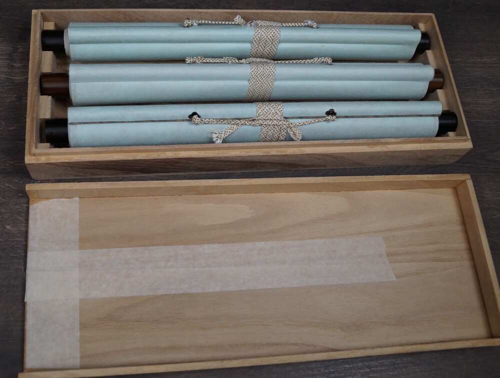Alle drei zusammengerollten Triptychon-Drucke nach Miyamoto Musashi mit Papierummantelung und Kordelverschluss in der geoeffneten Holzbox
