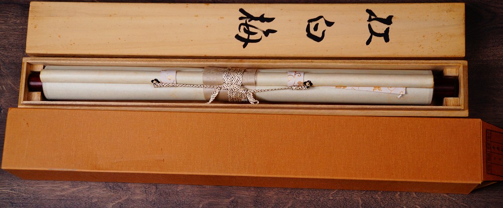 Zusammengerolltes und mit Kordel verschnuertes Kakemono Fruehlingsboten von Koizumi Kogetsu in der geoeffneten Aufbewahrungsbox mit der Tuschebeschriftung Kohaku-ume auf dem Deckel