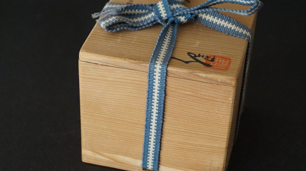 Geschlossene Aufbewahrungsbox mit blau-weissem Band und Kuenstlersiegel des Guinomi aus Shino-Keramik von Takeshi Kato
