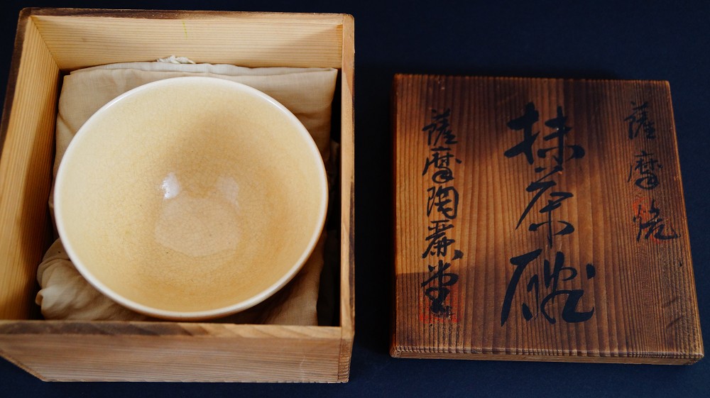 Chawan aus Satsuma-Keramik von Gyokusen Nozaki in Tuch gehuellt in der geoeffneten Aufbewahrungsbox mit der Beschriftung Satsuma-yaki Matcha-Chawan