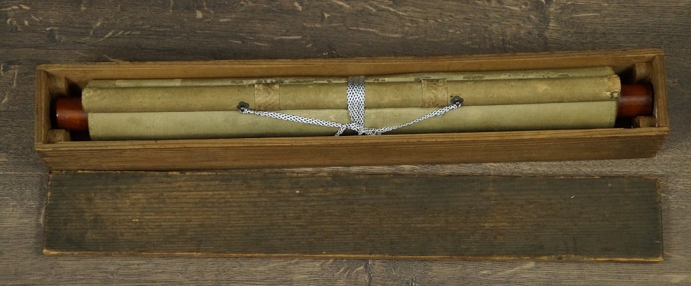 Das zusammengerollte und mit Kordel verschnuerte Kakemono liegend in der geoeffneten Aufbewahrungsbox