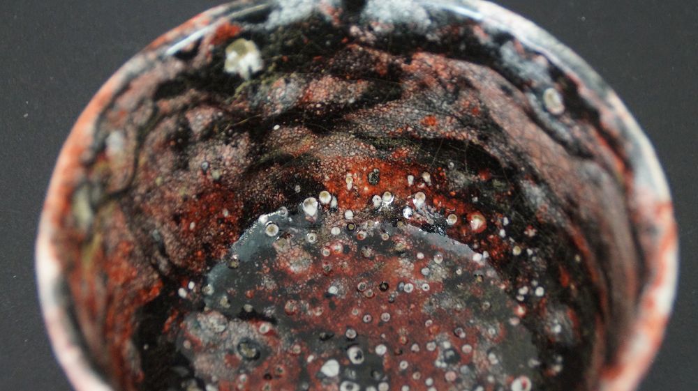 Nahaufnahme der bunt gesprenkelten Innenglasur der Chawan Teeschale aus Raku-Keramik