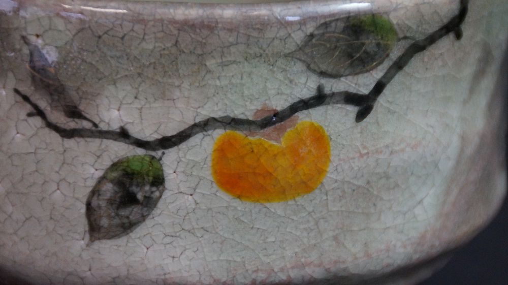 Nahaufnahme des handgemalten Kakizweigs mit oranger Frucht und gruenen Blaettern der Chawan aus Kyoto-Keramik