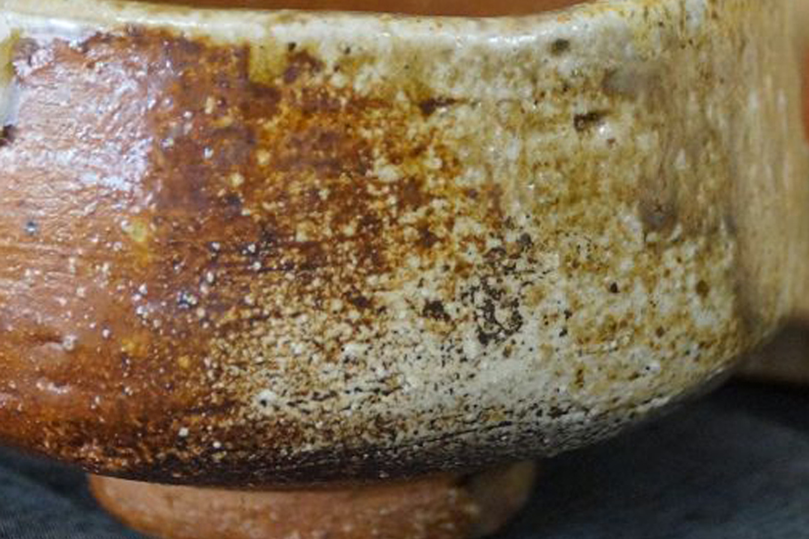 Nahaufnahme der Wandung einer Shigaraki-Teeschale mit rauer, ascheüberzogener Oberfläche, rotbrauner Brandzone und Fußring