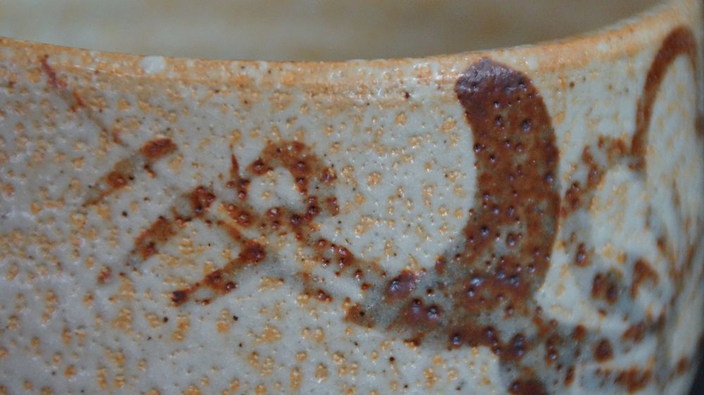 Nahaufnahme des rostroten Pinselmotivs am Rand der Chawan aus Shino-Keramik