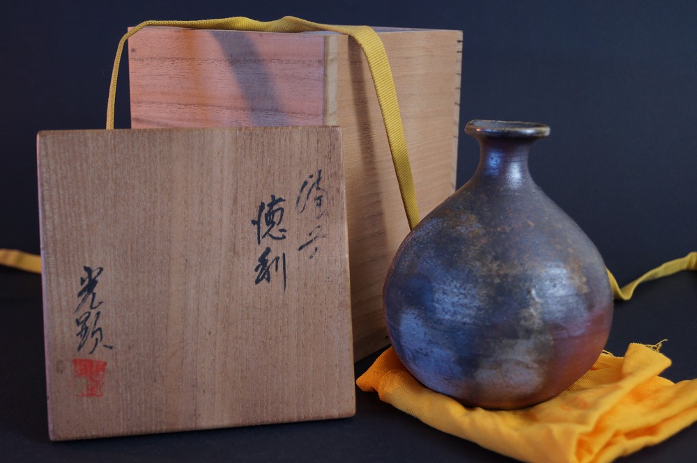 La botella de sake ante la caja de conservación firmada con sello rojo