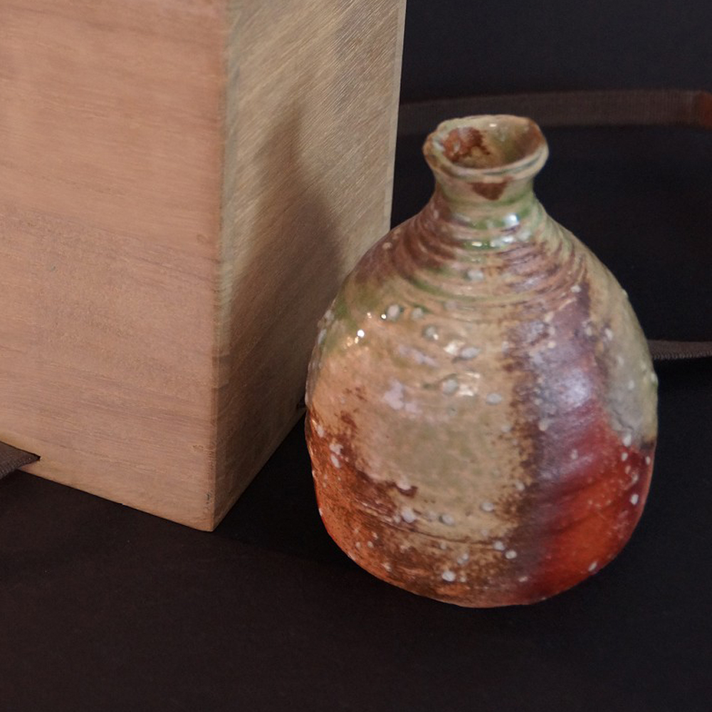 Vorschau-Nahaufnahme der Shigaraki Sake-Flasche mit gruen-rostroter Biidoro-Glasur neben der Aufbewahrungsbox