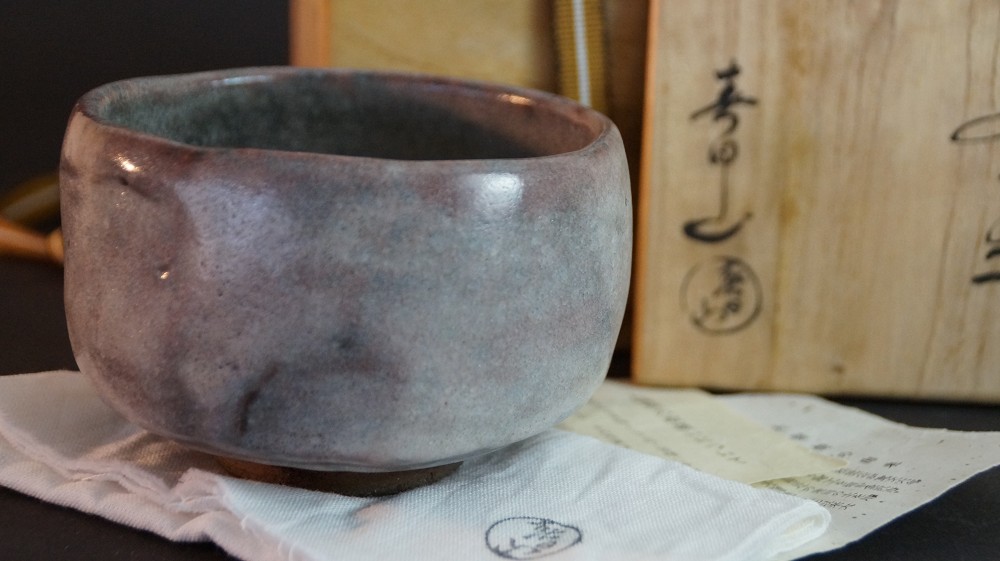 Seitenansicht des Chawan aus Ohi-Keramik vor der beschrifteten Aufbewahrungsbox von Kaihatsu Bunmei