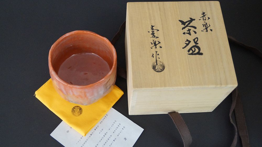 Chawan Teeschale mit Tee neben der beschrifteten Aufbewahrungsbox Akaraku Chawan und handschriftlichem Echtheitszertifikat