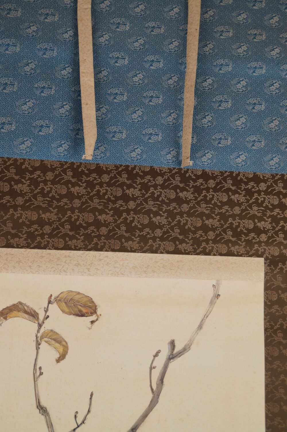 Detailansicht der Seidenmontierung mit blauem Blumenmuster, Brokatband und Aufhaengebaendern des Kakemono Wildschwein im Herbstlaub