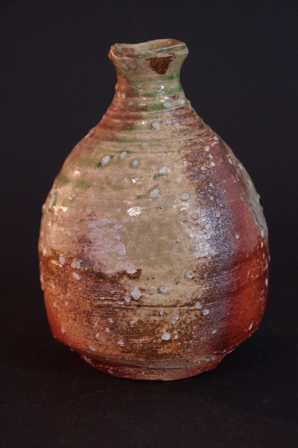 Frontalansicht der handgetoepferten Shigaraki Sake-Flasche mit gruenem Hals und rostroter Ascheanflug-Glasur