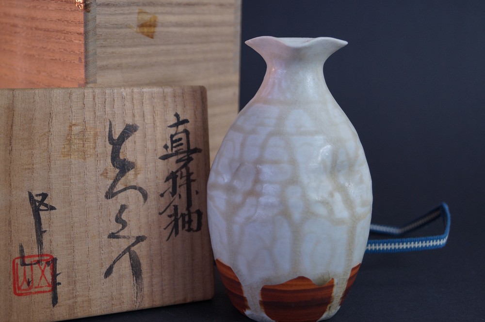 Die Sake Flasche vor der signierten Aufbewahrungsbox mit Kalligrafie und rotem Siegel