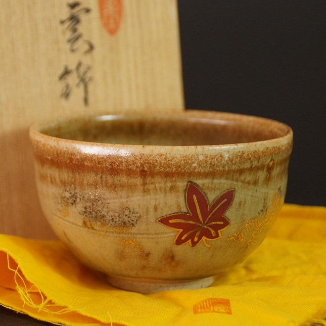 Chawan mit rotem Ahornblatt-Motiv auf gelbem Tuch vor der Aufbewahrungsbox