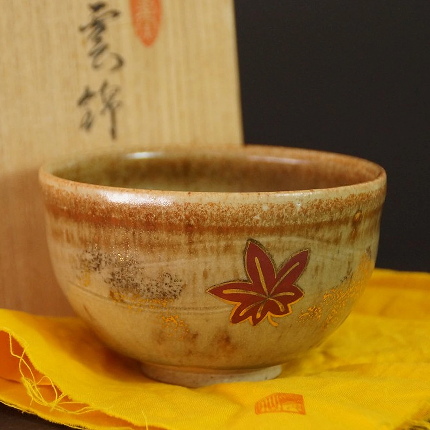 Chawan à motif de feuille d'érable rouge sur tissu jaune devant la boîte de rangement