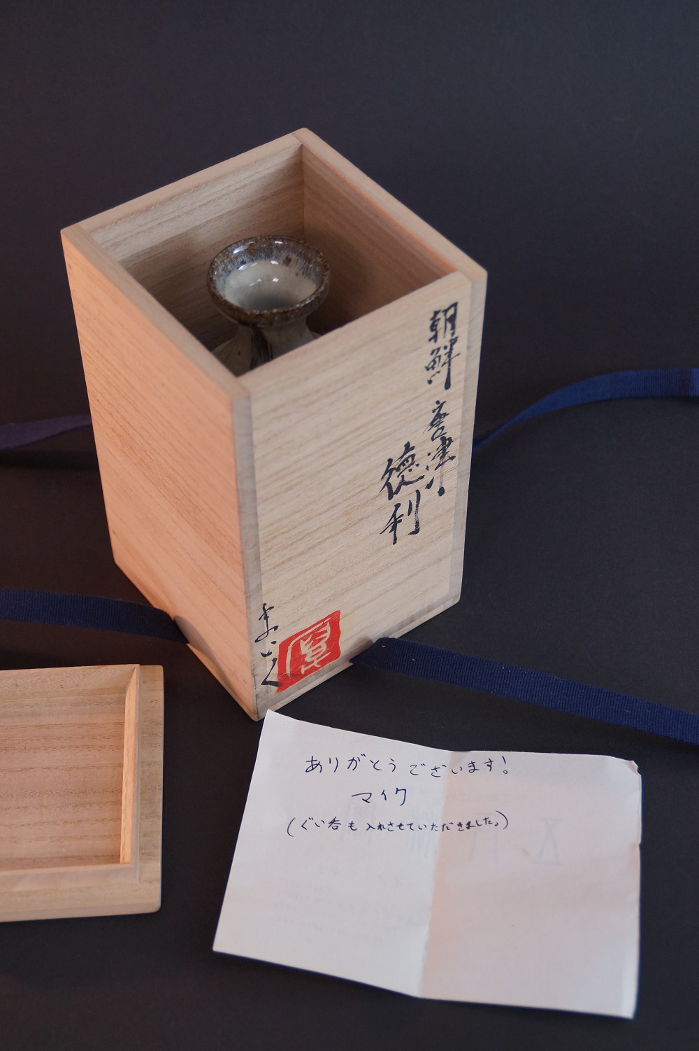 Die Sake Flasche stehend in der geoeffneten Aufbewahrungsbox mit persoenlichem Dankschreiben des Toepfers