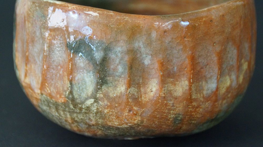 Nahaufnahme des gerippten Randes mit orange-gruener Raku-Glasur der Chawan Teeschale aus Raku-Keramik