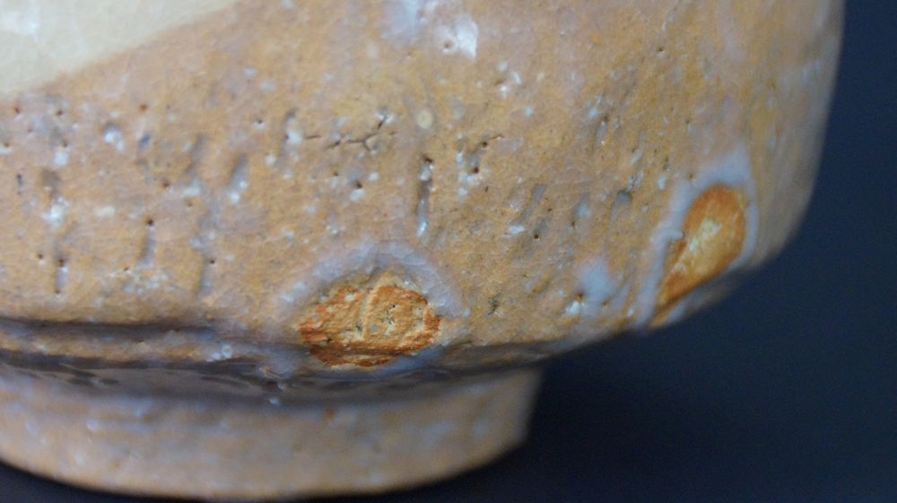 Extreme Nahaufnahme der genarbten Glasurstruktur mit orangefarbenen Einsprengseln der Chawan Teeschale aus Raku-Keramik