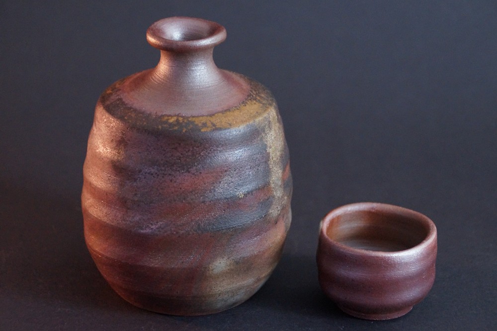Frontalansicht der handgetoepferten Bizen Sake Flasche mit dazugehoerigem Guinomi