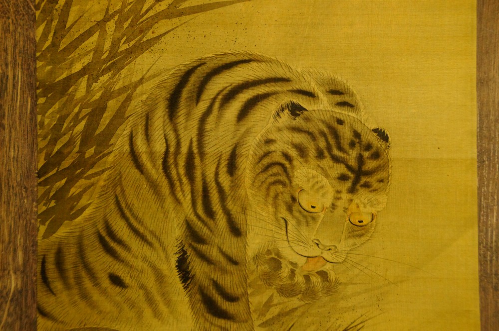 Nahaufnahme des gestreiften Tigerkopfs mit Ohr und wachem Blick auf goldener Seide