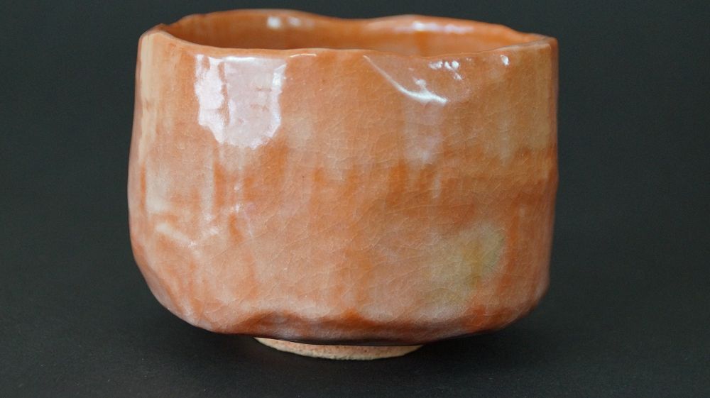 Chawan Teeschale aus Raku-Keramik von Ichiraku Nishimura in der Gesamtansicht mit glaenzender orangefarbener Glasur