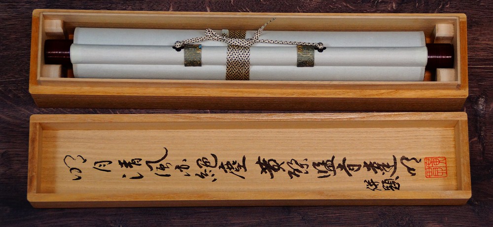 Zusammengerolltes Kakemono mit Kordelverschnuerung in der Aufbewahrungsbox mit beschriftetem Deckel
