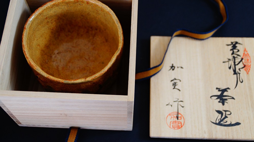 Chawan aus Seto-Keramik von Takamichi Kato neben dem geoeffneten Deckel der Aufbewahrungsbox mit Tuschebeschriftung und rotem Kuenstlersiegel