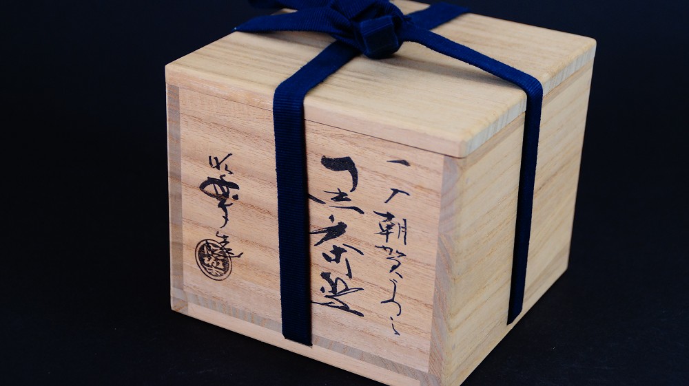 Geschlossene Aufbewahrungsbox der Chawan aus Raku-Keramik von Shoraku Sasaki mit Tuschebeschriftung und rotem Kuenstlersiegel, verschnuert mit dunkelblauem Band