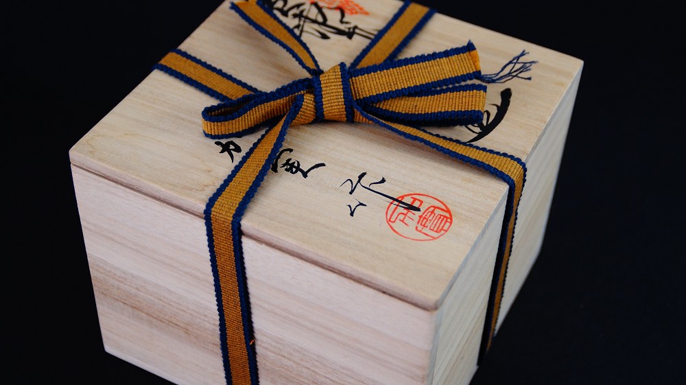 Geschlossene Aufbewahrungsbox der Chawan aus Seto-Keramik von Takamichi Kato mit Tuschebeschriftung und rotem Kuenstlersiegel, verschnuert mit gelb-blauem Band