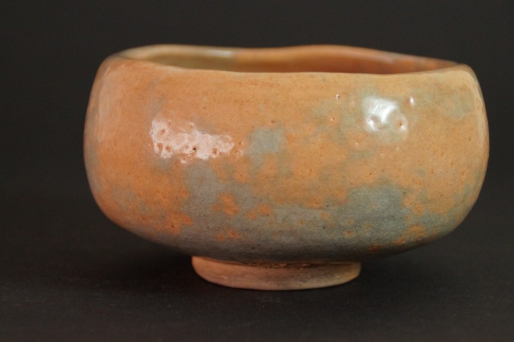 Vista laterale del chawan con smalto screziato arancio-verde davanti alla scatola