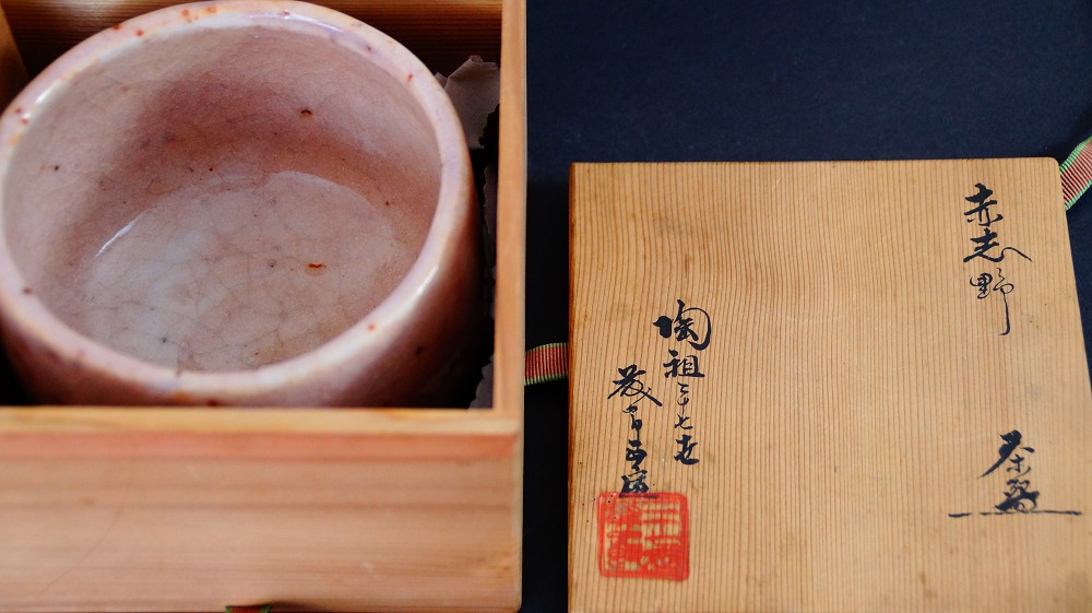 Chawan aus Shino-Keramik von Masayoshi Kato neben dem geoeffneten Deckel der Aufbewahrungsbox mit der Tuschebeschriftung Aka-Shino Chawan