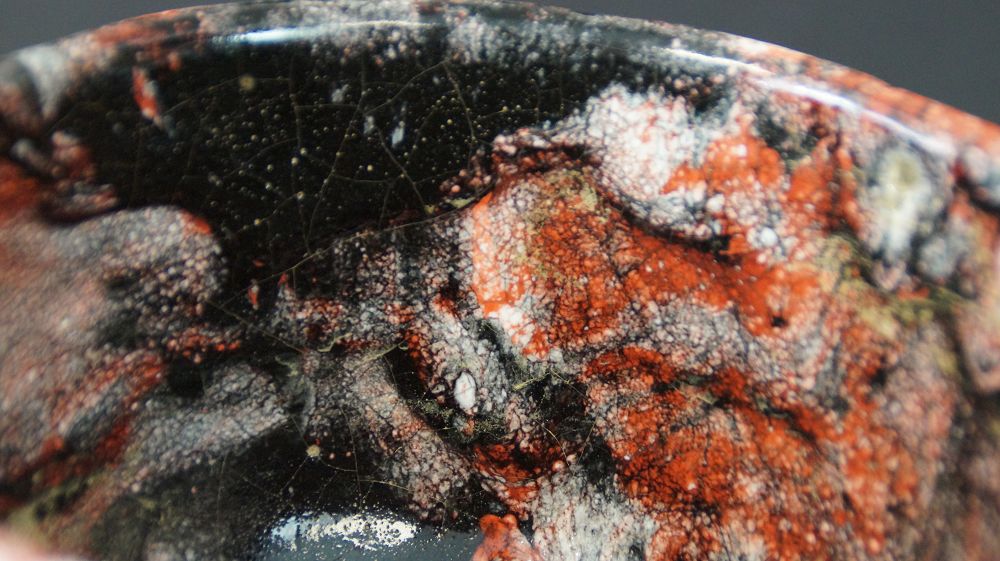 Extreme Nahaufnahme der rot-schwarz-weissen Glasurstruktur der Chawan Teeschale aus Raku-Keramik