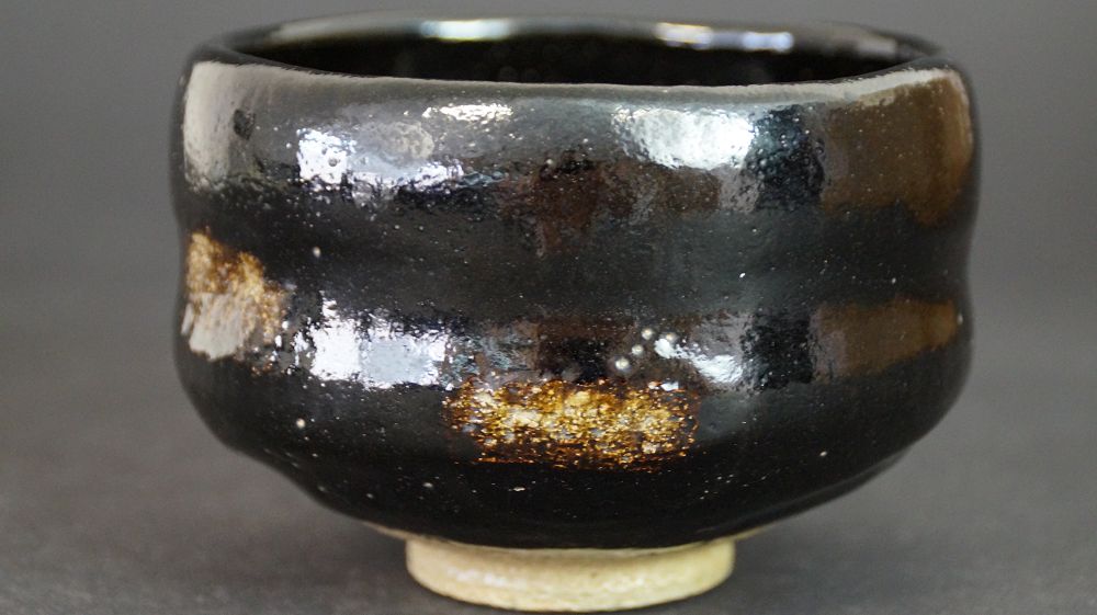 Autre vue du chawan en céramique Raku à glaçure noire avec taches de glaçure dorées sur le bord