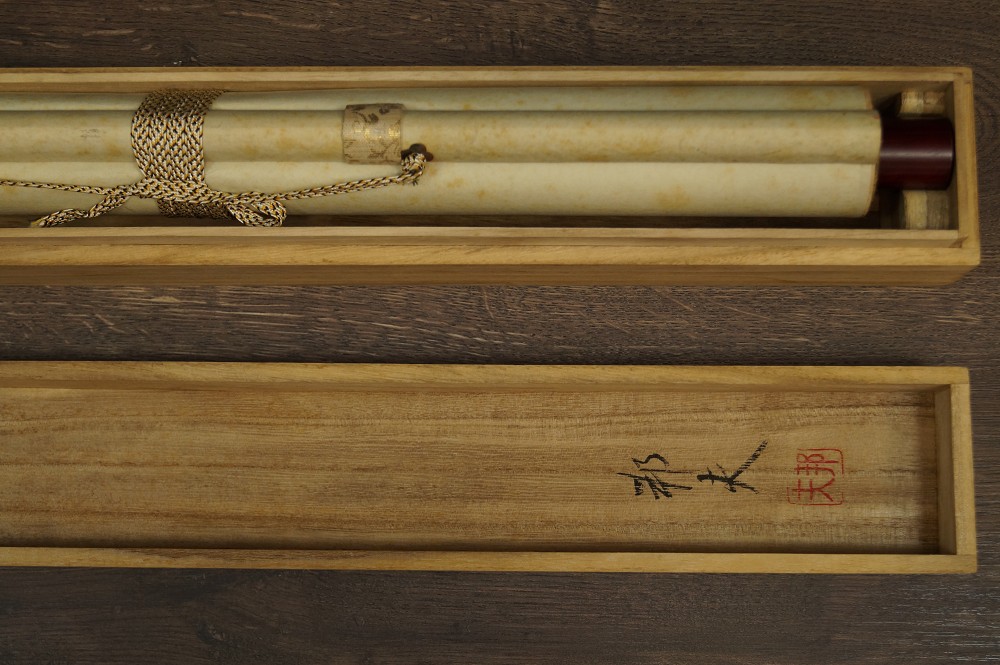 Zusammengerolltes Rollbild in geoeffneter Holzbox mit Kordel