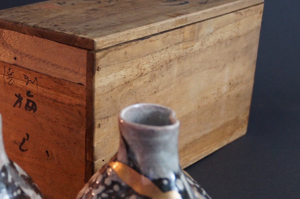 Nahaufnahme der Flaschenmuendung vor der unscharf sichtbaren Aufbewahrungsbox mit Kalligrafie