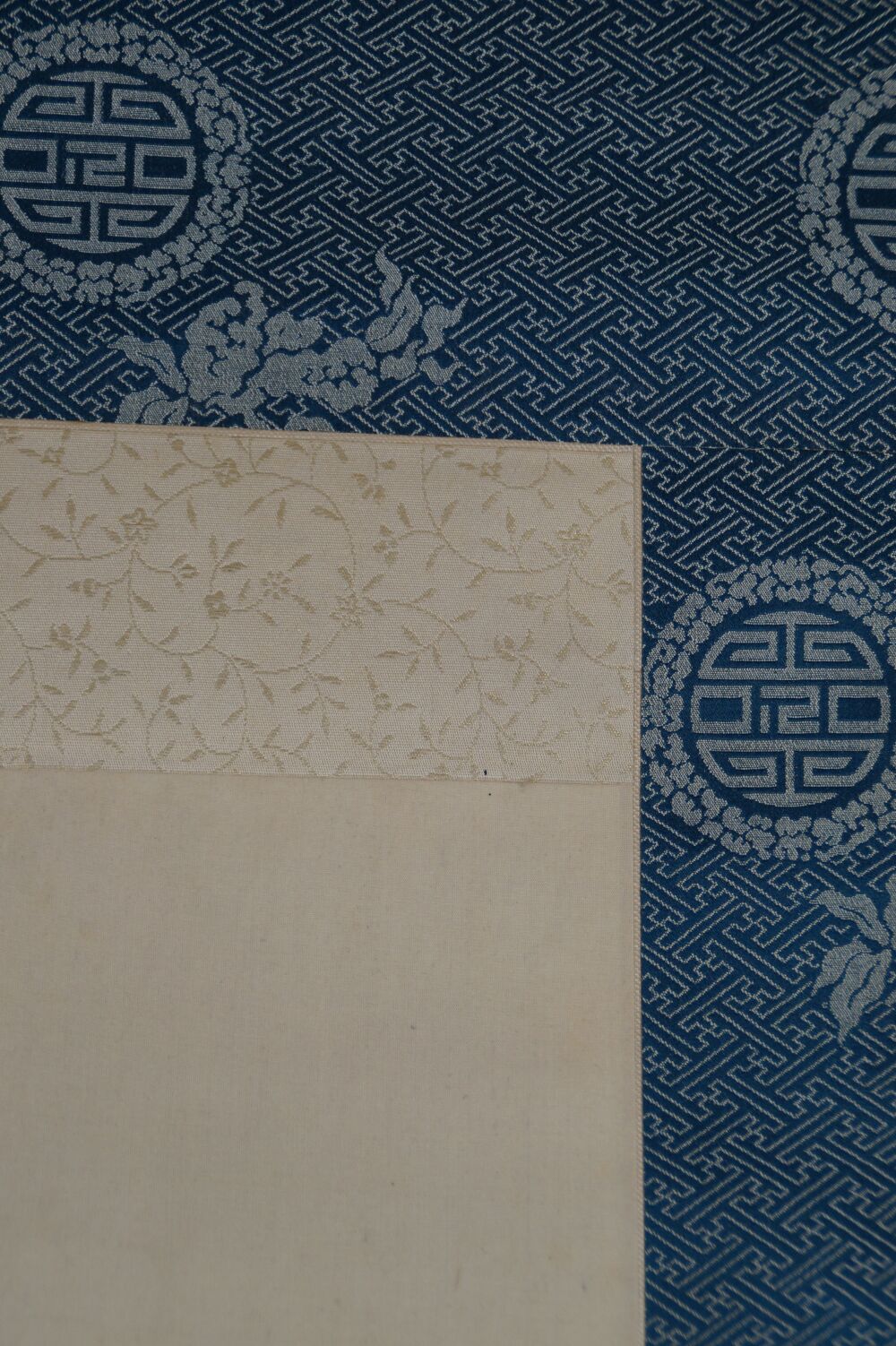 Detailansicht der blauen Seidenmontierung mit Rundmedaillon-Muster und cremefarbenem Bildrand des Kakemono Japanische Aubergine