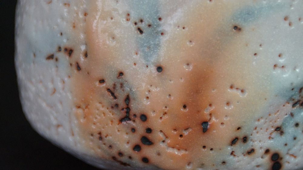 Extreme Nahaufnahme der pastellfarbenen Glasurtextur der Chawan aus Shino-Keramik mit rotbraunen Sprenkeln