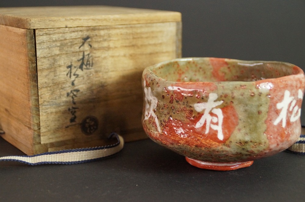 Chawan mit in die Glasur eingearbeiteten Schriftzeichen vor der beschrifteten Aufbewahrungsbox