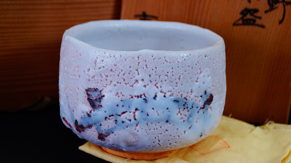 Chawan aus Shino-Keramik von Jyuzo Sato vor der Aufbewahrungsbox auf gelbem Tuch
