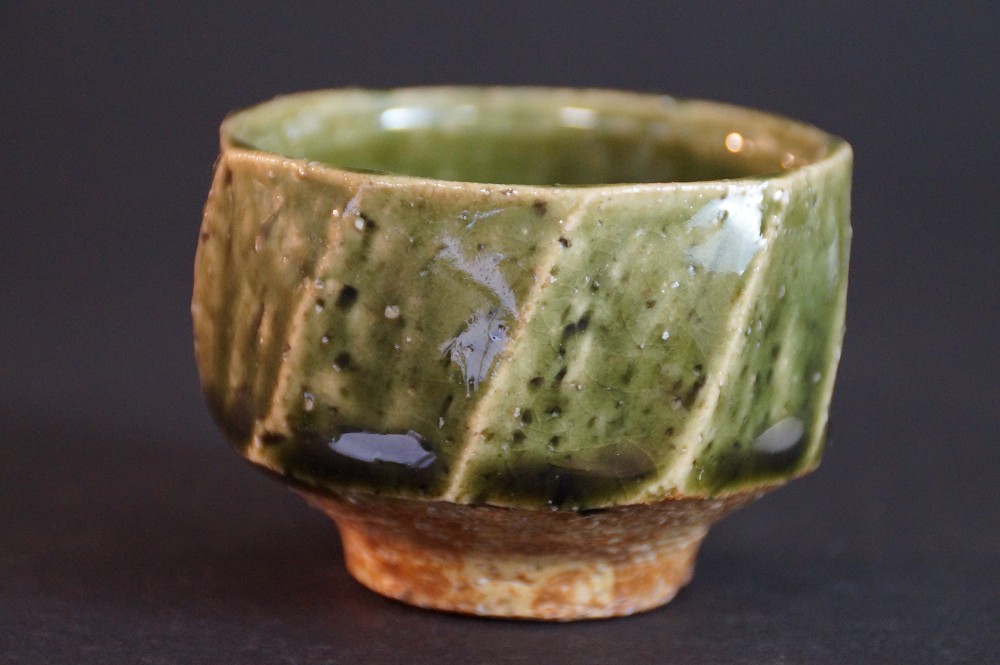 Seitenansicht der facettierten Sake Schale mit kupfergruener Glasur ueber cremefarbenem Scherben