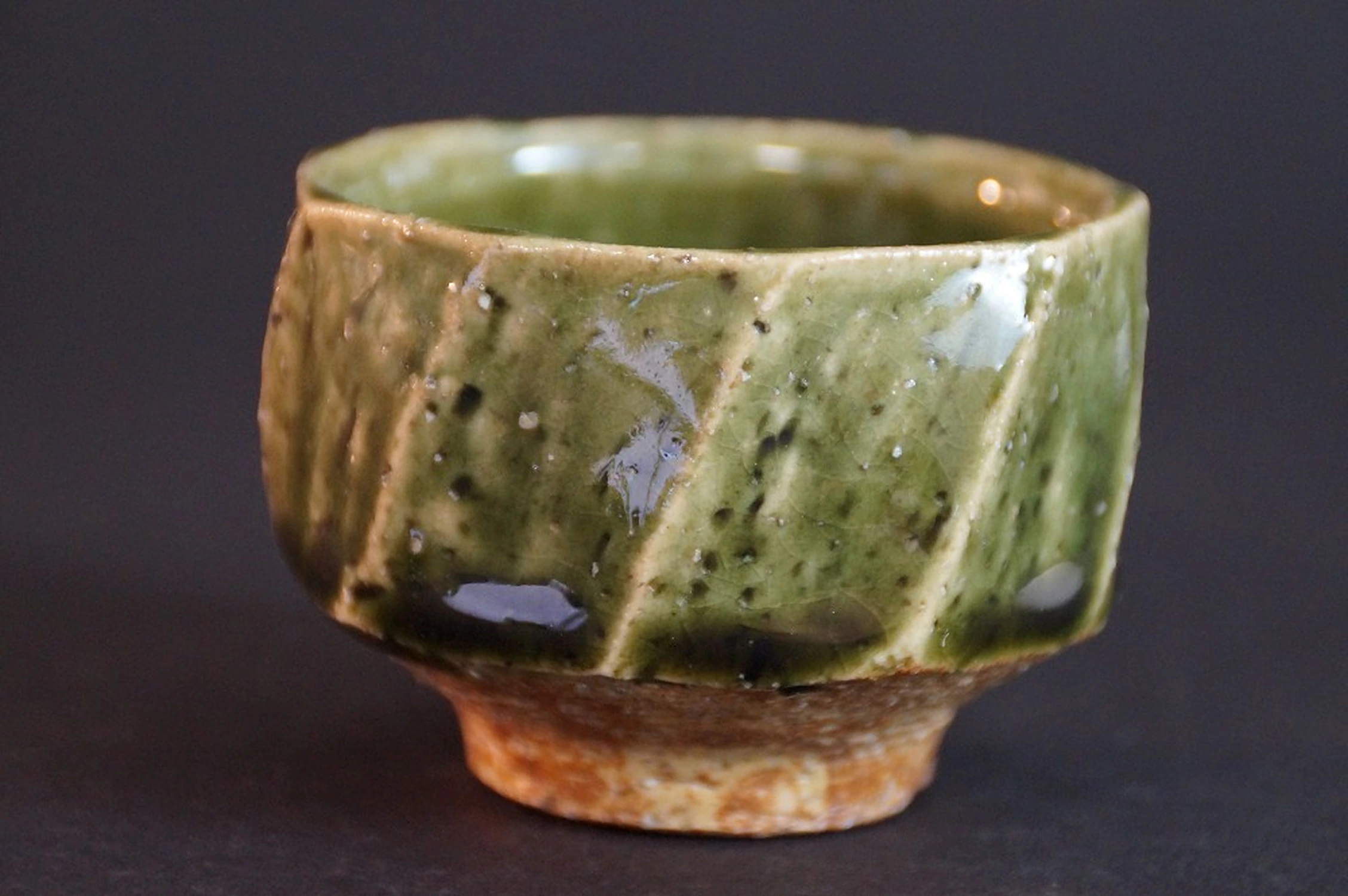 Vue de côté de la coupelle à saké facettée avec glaçure vert cuivré sur pâte crème
