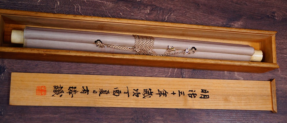 Zusammengerolltes Kakemono mit Kordelverschnuerung in der Aufbewahrungsbox mit beschriftetem Deckel