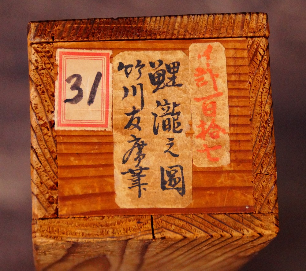Nahaufnahme des Deckels der Aufbewahrungsbox mit der Tuschebeschriftung Koi Taki no Zu und der Signatur Takekawa Tomohiro