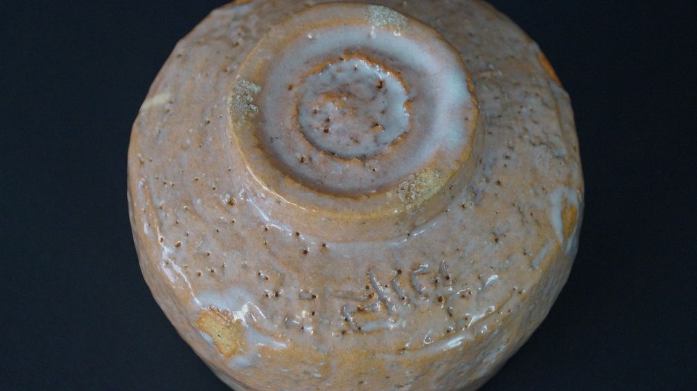 Detailansicht des spiralfoermig gedrehten Standfusses mit eingeritzter Signatur der Chawan Teeschale aus Raku-Keramik
