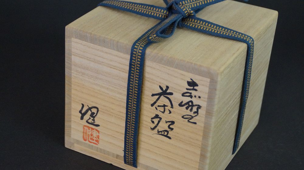 Geschlossene, mit blau-goldenem Band verschnuerte Aufbewahrungsbox der Chawan aus Shino-Keramik