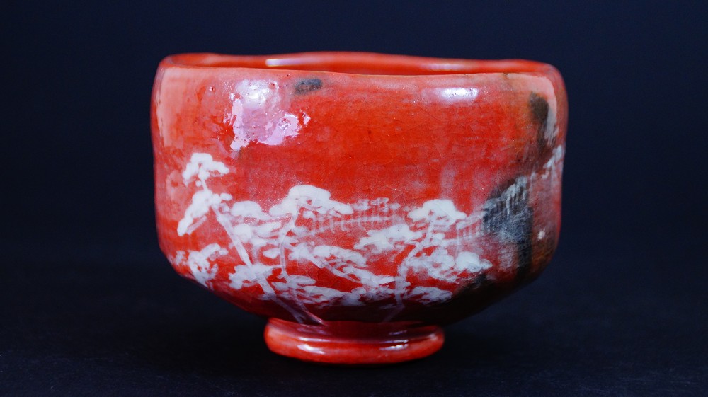 Chawan aus Raku-Keramik von Waraku Kawasaki in der Frontalansicht mit leuchtend roter Glasur und weiss gemaltem Kiefernmotiv