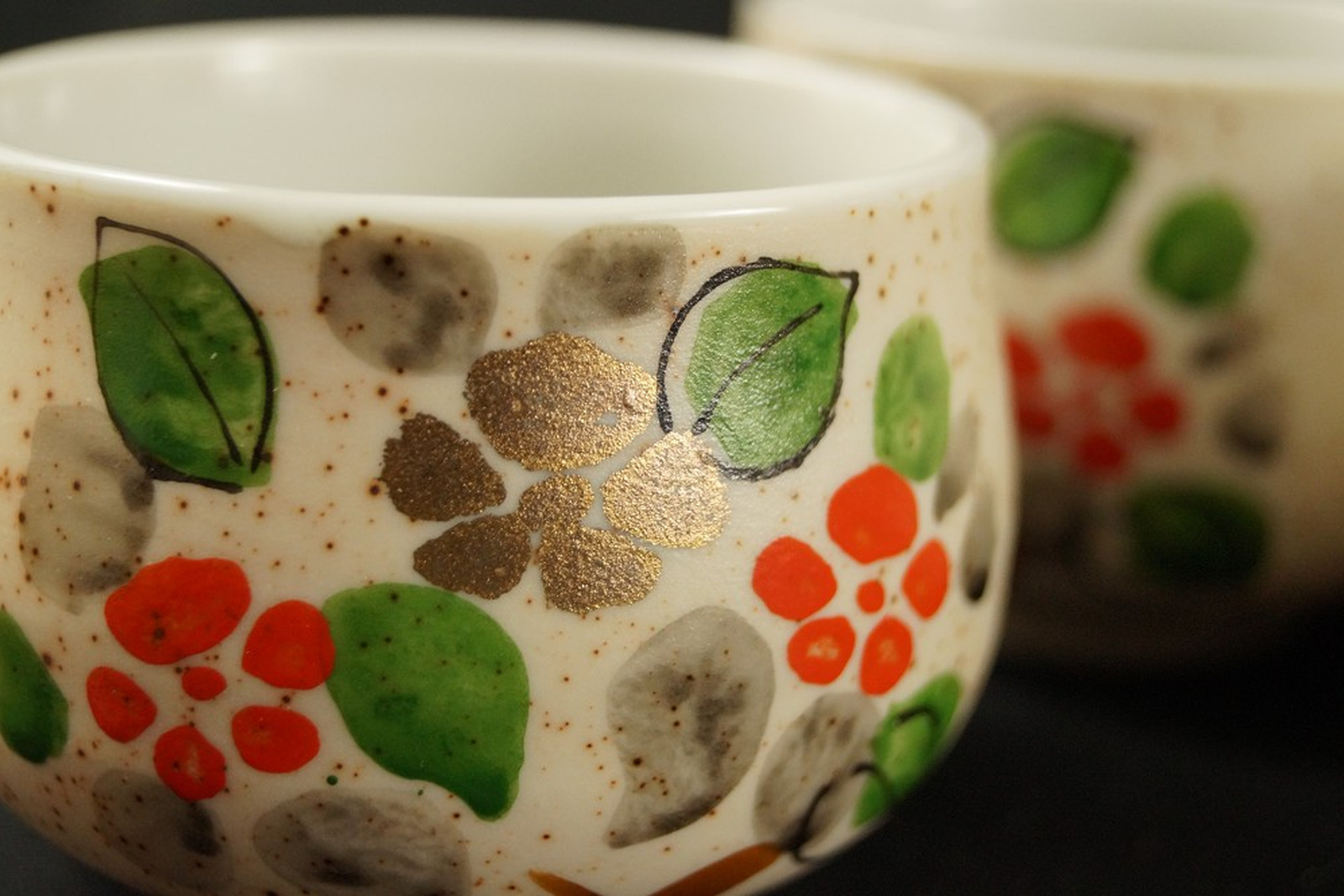 Japanische Teeschale aus Imari-Porzellan mit handgemalten roten Blüten, grünen Blättern und einer goldenen Blüte auf cremeweißem, fein gesprenkeltem Grund