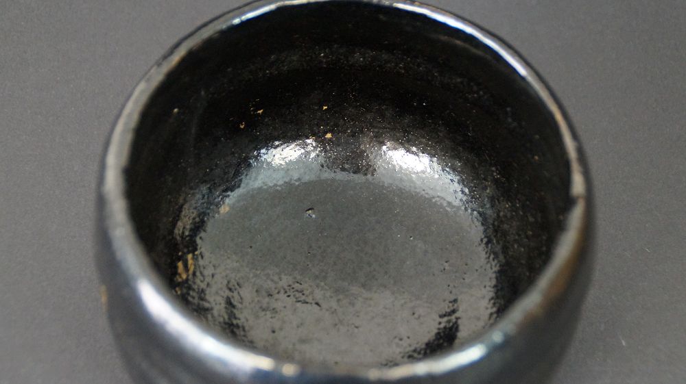 Zbliżenie błyszczącego czarnego szkliwa wewnętrznego czarki do herbaty chawan z ceramiki Raku