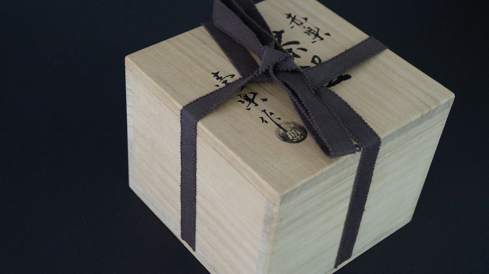 Geschlossene Aufbewahrungsbox mit Baumwollband und Kuenstlersiegel der Chawan Teeschale aus Raku-Keramik